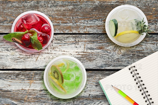 Top view of three glasses with cool lemonade on wooden table near notebook