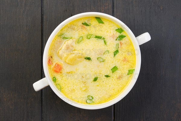 Overhead view of a bowl with hake soup with cream and carrot on a table