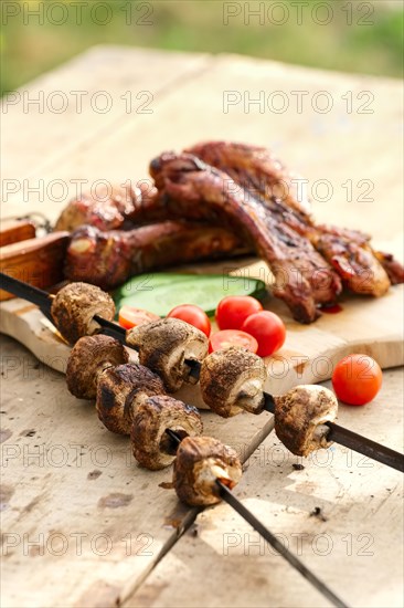 Grilled ribs and champignon on skewer served with fresh cucumber and tomato on wooden table outdoor