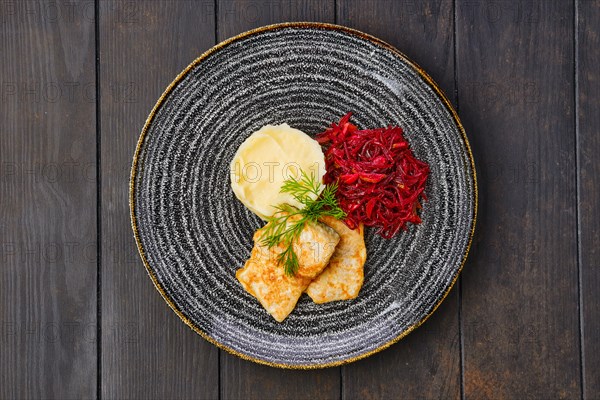Top view of fried hake in breading with mashed potato and roasted beetroot on dark wooden table