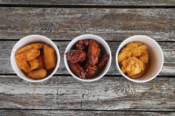 Top view of three cardboard containers with fried chicken wings on wooden table