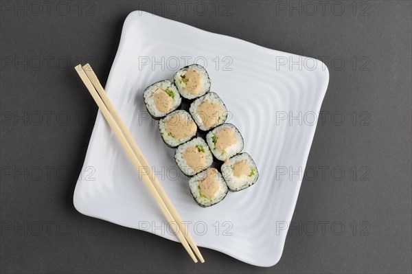 Chicken roll with nori and nut sauce on white plate near hashi