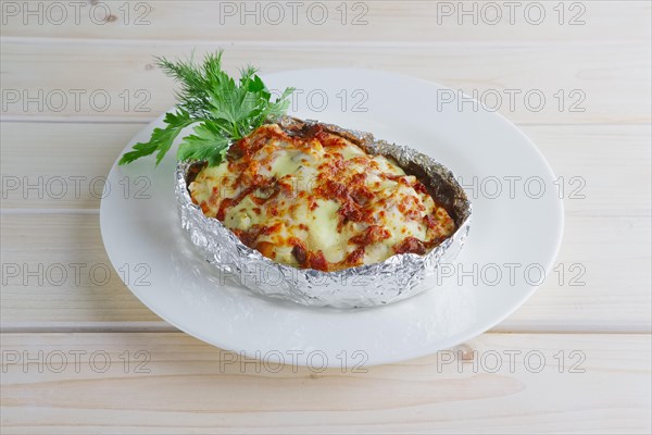Meat baked in foil with vegetables and cheese on wooden table