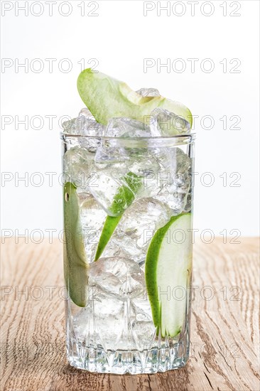 Glass of cold apple lemonade with ice on wooden table