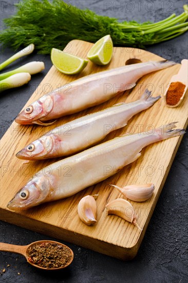 Raw fresh smelt fish on wooden cutting board with spice and herbs