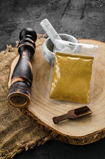 Wooden cross section with curry in plastic package and stone mortar and mill