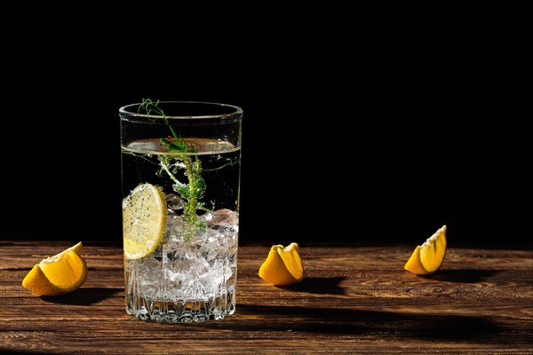 Carbonated cold water with ice and lemon casting a shadow on wooden table