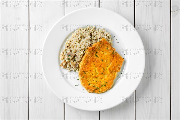 Top view of schnitzel with green buckwheat on white wooden table