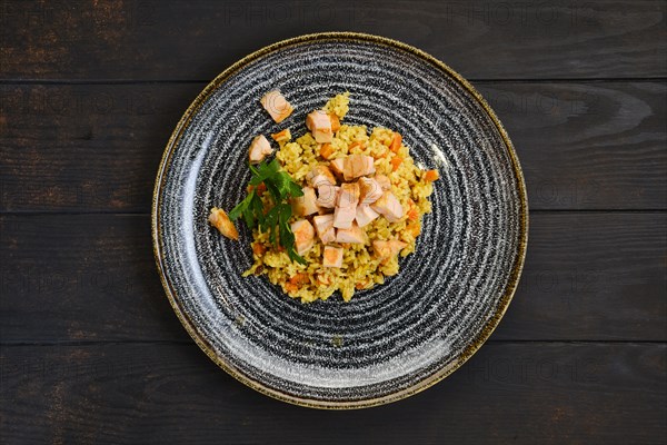 Top view of plate with risotto with ham and carrot on dark wooden table