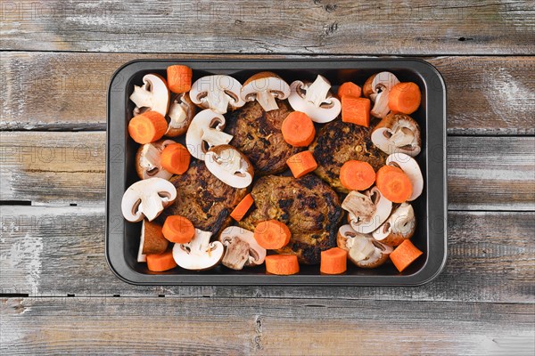 Lamb neck with champignon and vegetables baked in oven on wooden table