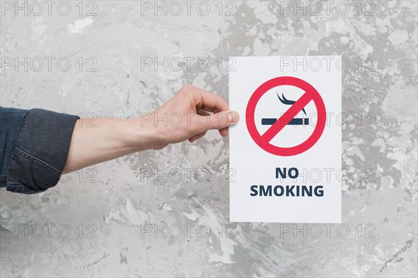 Male hand holding paper with no smoking sign text weathered wall