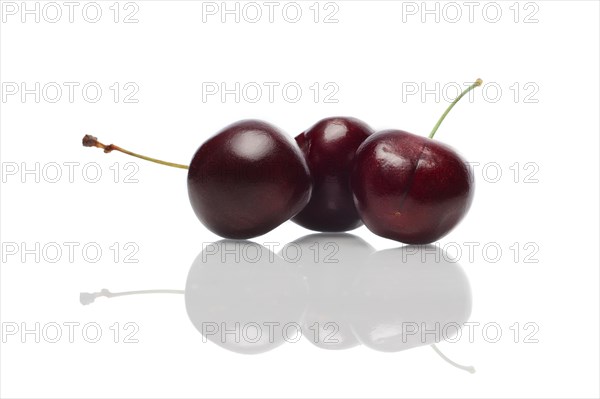 Three fresh cherries with reflection on glossy surface