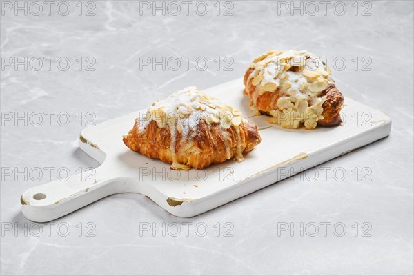 Crispy croissant with caramel and peanut shavings on white serving board on marble surface