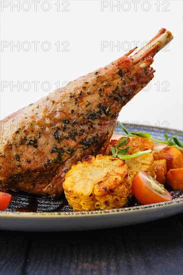 Close up view of roaster turkey leg with fried pumpkin and grilled corn decorated with tomato