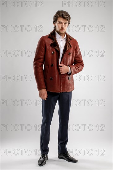 Brutal handsome unshaven man with beard and moustache in sheepskin coat with fur collar