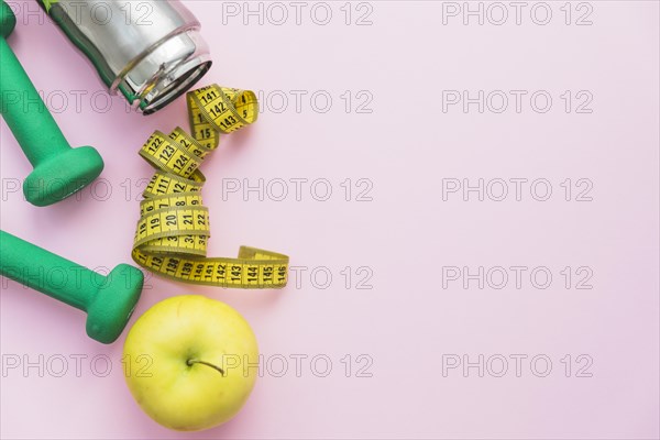 Dumbbells water bottle measuring tape apple pink background