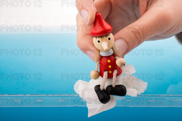 Hand holding wodden puppet Pinocchio on in blue water