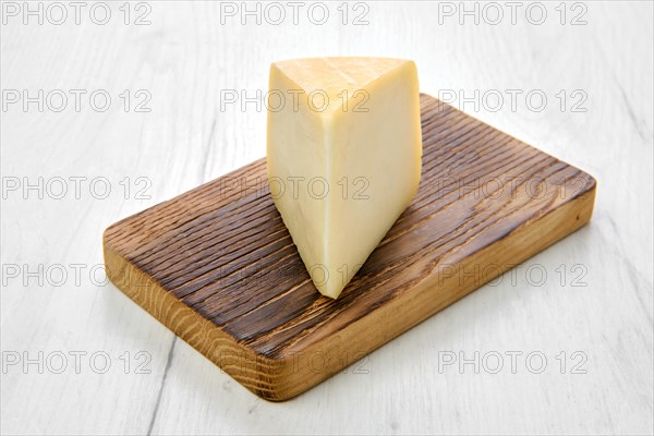 Triangular piece of goat cheese on wooden cutting board on black background