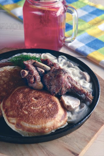 Fried in oven rabbit with fritters and onion sauce. Cast iron pan on wooden cutting board and glass with cranberry juice