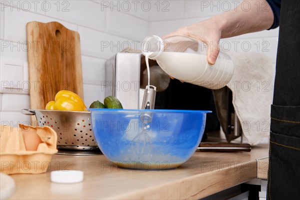 Closeup view of hands of a man pouring milk in a bowl with beaten eggs to make an omelet