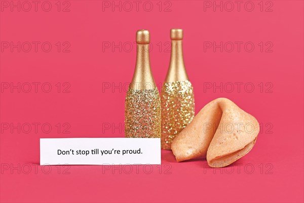 Fortune cookie and champagne bottles with motivational text 'Don't stop till you're proud' on paper on pink background