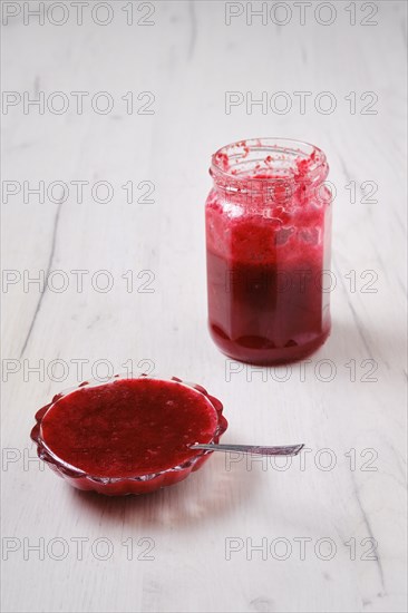 Jar and saucer with cherry jam on white wooden background