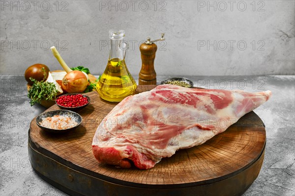 Raw lamb leg chump on with ingredients on wooden stump
