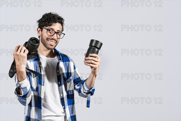 Portrait of smiling photographer man showing a camera and lens on isolated background. Smiling young man holding a camera isolated