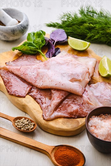 Raw fresh unpeeled squid on wooden cutting board with spice and herbs