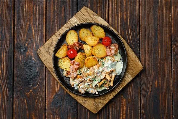 Top view of potato wedges with chanterelles and pork in cast iron skillet