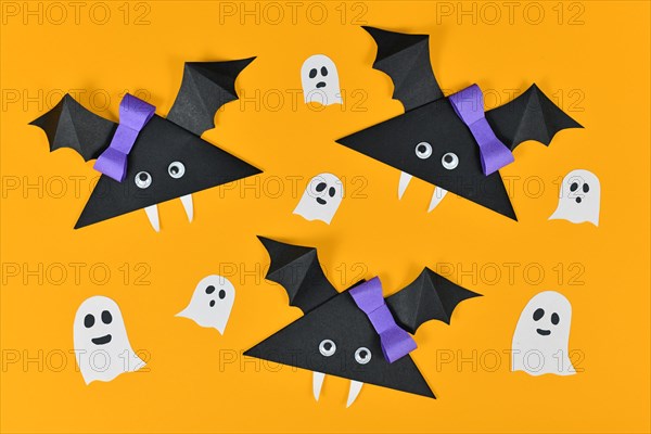 Origami paper vampire bats with googly eyes and ghosts and spiders on yellow Halloween background