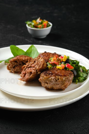 Closeup view of fried veal meatballs on a plate with basil and tomato