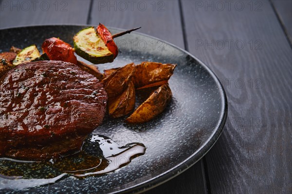 Closeup view of juicy beef steak with potato wedges and grilled vegetables on skewer