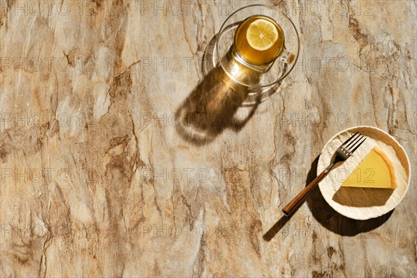 Top view of piece of lemon tart with tea under direct sunlight with hard shadows on the table