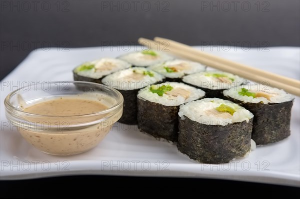 Chicken roll with nori and nut sauce on white plate near hashi