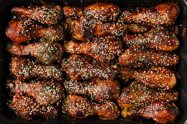 Closeup view of baked chicken legs with spicy sauce on a baking tray