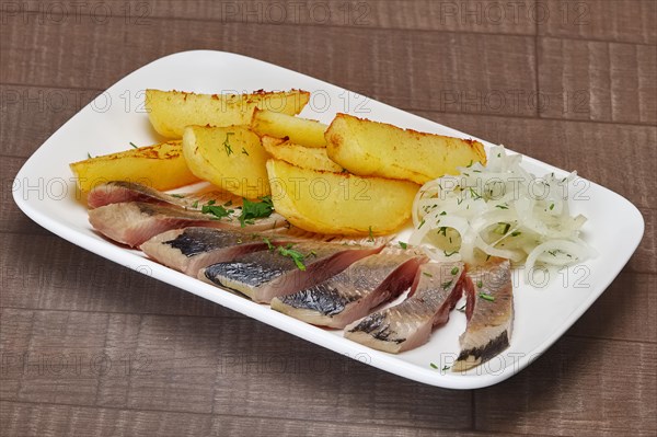 Plate with pickled herring and onion with potato wedges on wooden table