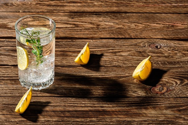 Carbonated cold water with ice and lemon casting a shadow on wooden table