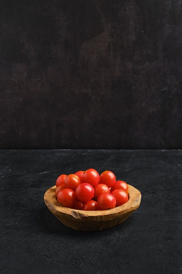 Fresh tomato cherry in wooden bowl on dark background