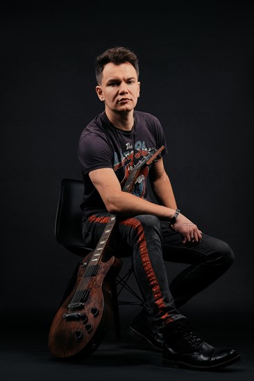 Low key portrait of musician sitting on chair with electro guitar