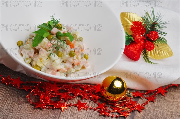 Russian traditional salad olivier with pea on wooden table near new years decorations