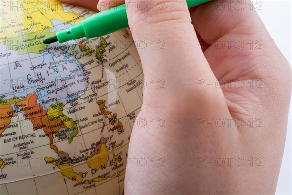 Hand holding a grren color pen on a little model globe on white