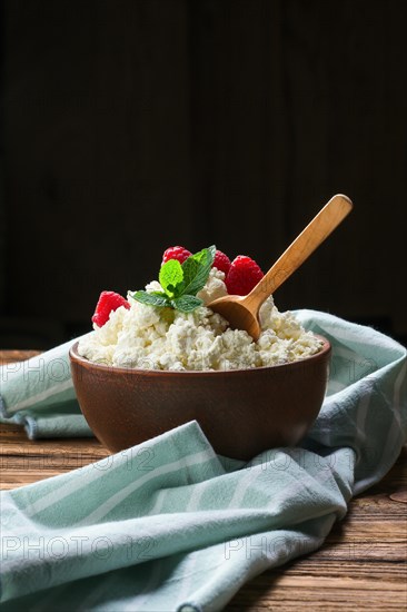 Fresh cottage cheese with raspberries and wooden spoon in clayware on wooden table