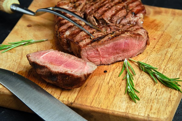 Close up view of juicy steak on wooden cutting board over black background
