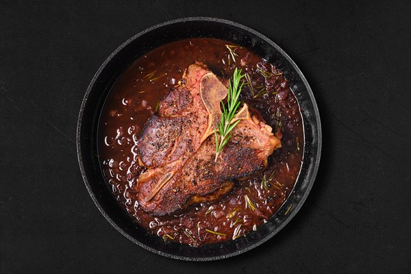 Overhead view of porterhouse steak in wine sauce in frying pan