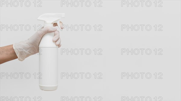 Hand with glove holding cleaning solution in bottle with copy space