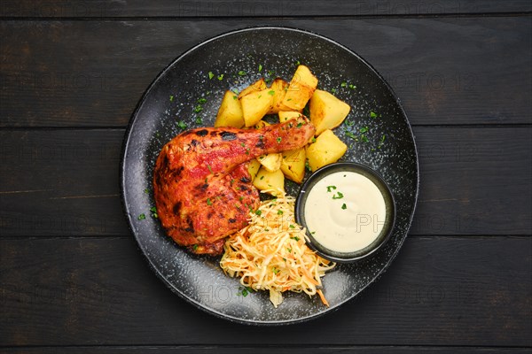 Top view of whole roasted chicken thigh with potato wedges and pickled cabbage