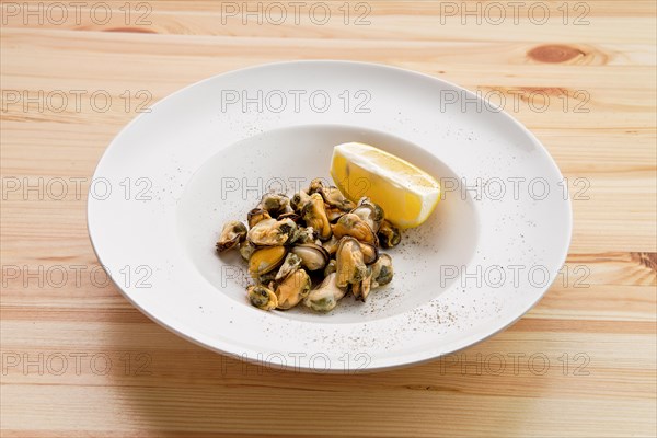 Plate with marinated mussels and slice of lemon on wooden table