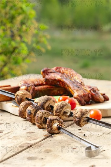 Grilled ribs and champignon on skewer served with fresh cucumber and tomato on wooden table outdoor