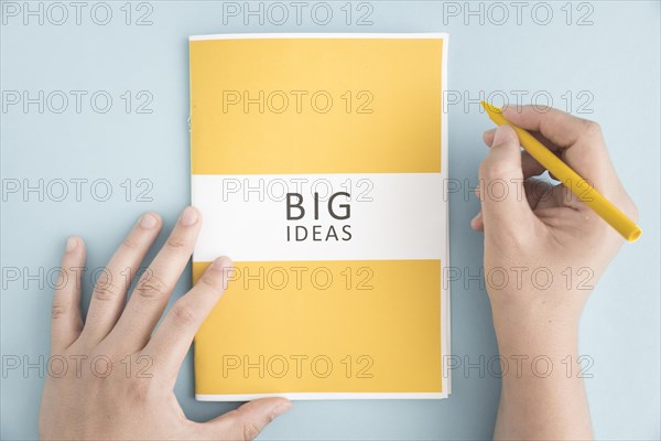 Close up person holding yellow crayon with big idea book blue background